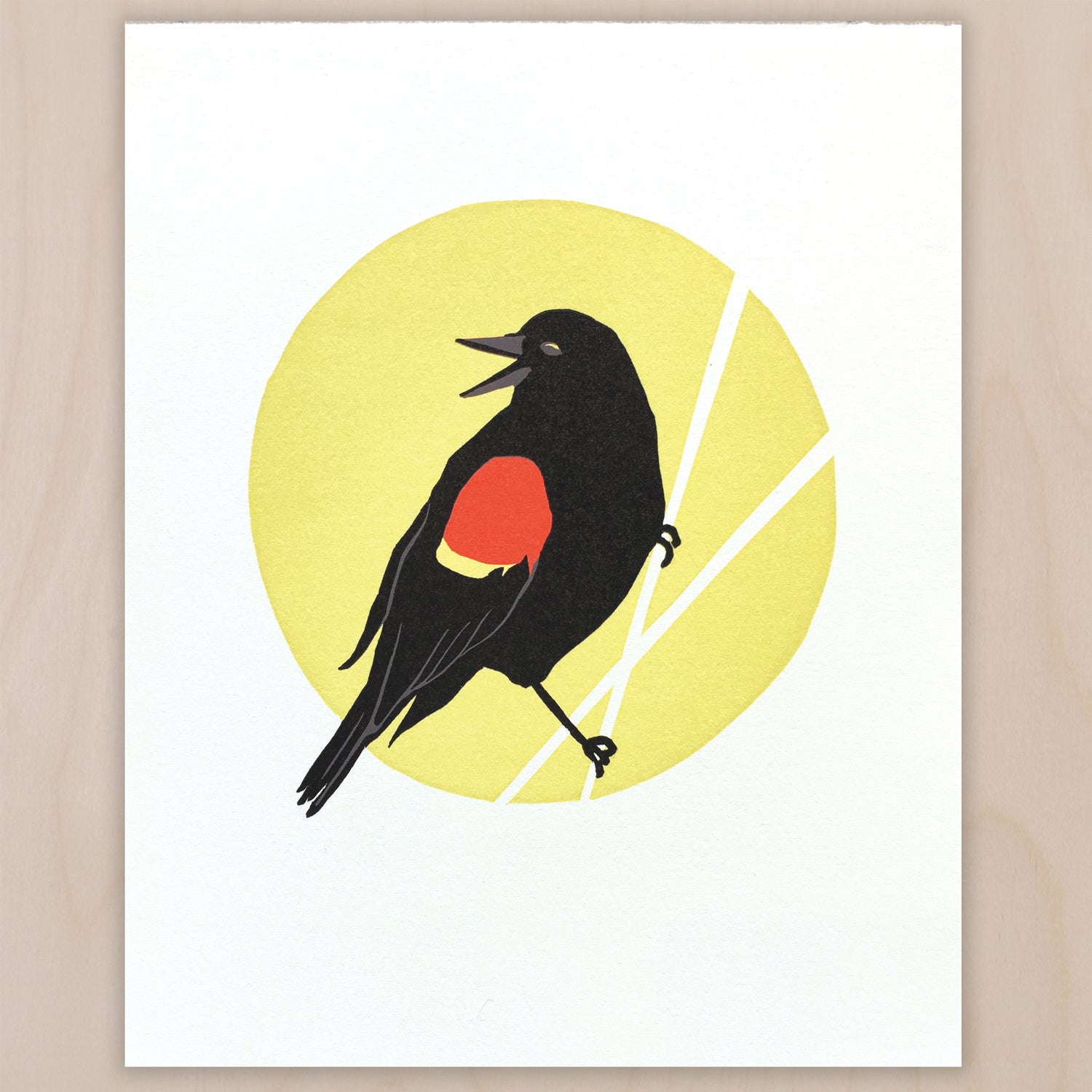 Linoleum block print on white paper showing a side-view of a Red-winged Blackbird, with it's head turned to the left and it's beak open. It is on a yellow circle that has white diagonal lines through it that look like reeds. It is holding onto one of these lines with its feet.